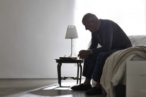 Elderly man sitting on bed looking serious