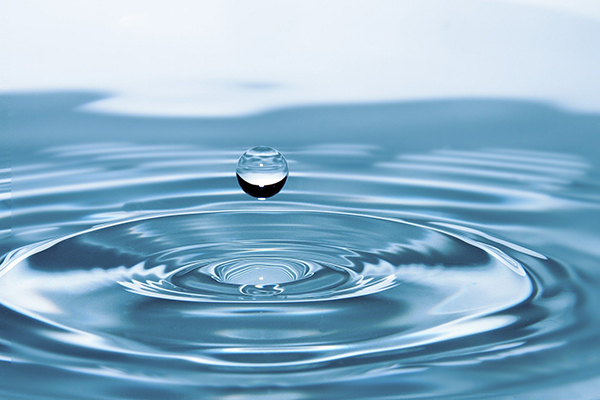 close up of a drop of water making ripples when it lands on the surface of water