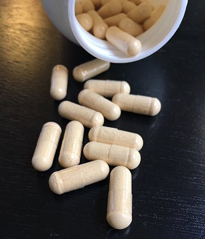 multivitamin capsules spilling out of a white bottle onto a dark surface