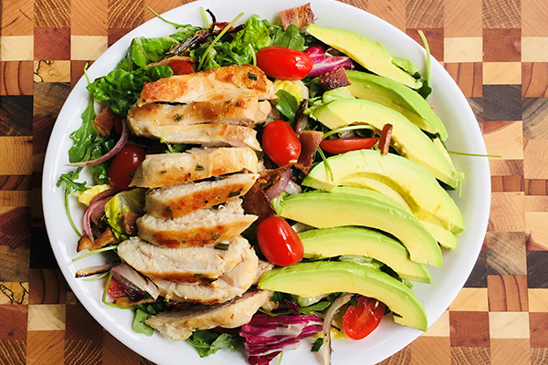 salad of mixed greens topped with slices of grilled chicken, avocados and cherry tomatoes