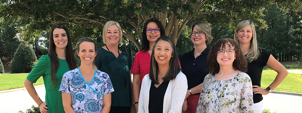 eight female pediatric care providers pictured with trees and greenery in the background 