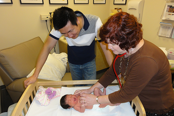 Female nurse practitioner examining newborn baby as proud dad observes