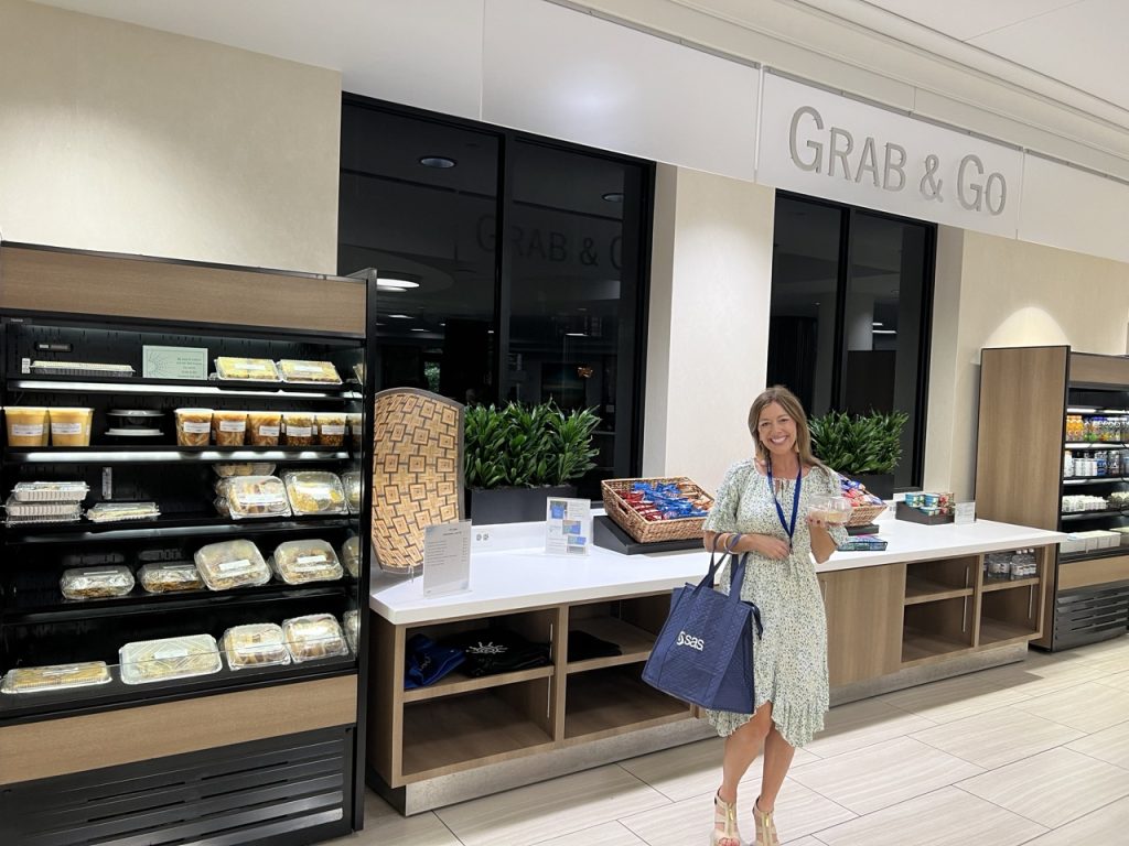 An employee smiles and holds a to-go lunch in front of the "grab and go" area. 