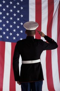 Man in U.S. Marine Corps Uniform who is saluting the Flag of the United States of America