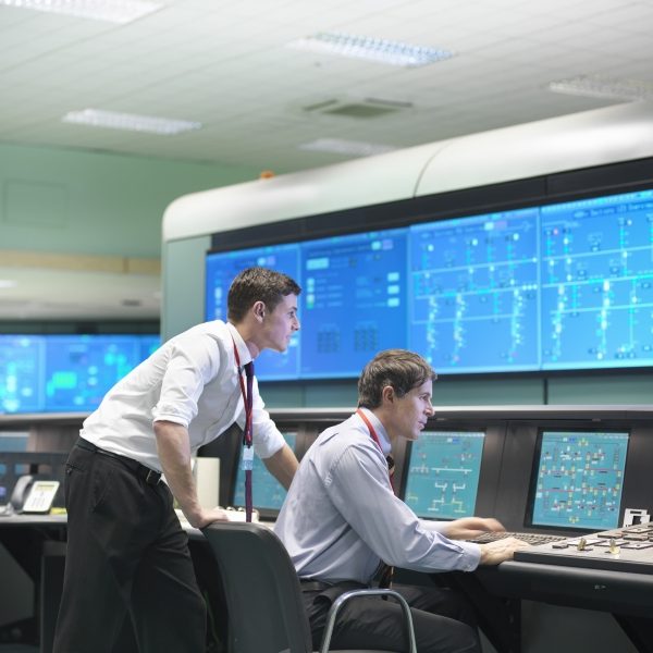 Two men viewing large monitors in a utility control room