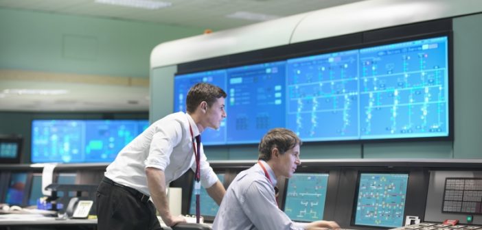 Two men viewing large monitors in a utility control room