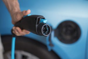 Power plug of electric car -- close up man's hand holding 3 pin power plug of a blue electric car 