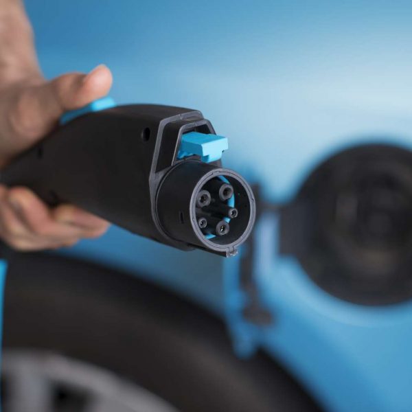 Power plug of electric car -- close up man's hand holding 3 pin power plug of a blue electric car
