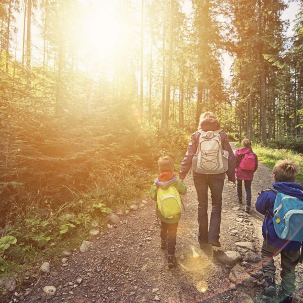 mom and three kids hiking in woods with backpacks