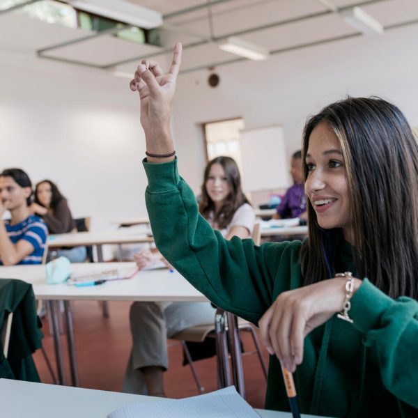 A high school student raising her hand in class ready to ask a question.