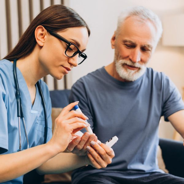 Healthcare professional assisting an elderly man with diabetes, performing a routine blood glucose test for home care monitoring