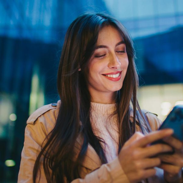 Camera moving around happy Caucasian female. Woman looking at mobile phone display and smiling from receiving funny message. Chatting online. Planning upcoming meeting with friend in city.