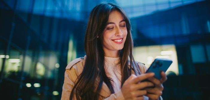 Camera moving around happy Caucasian female. Woman looking at mobile phone display and smiling from receiving funny message. Chatting online. Planning upcoming meeting with friend in city.