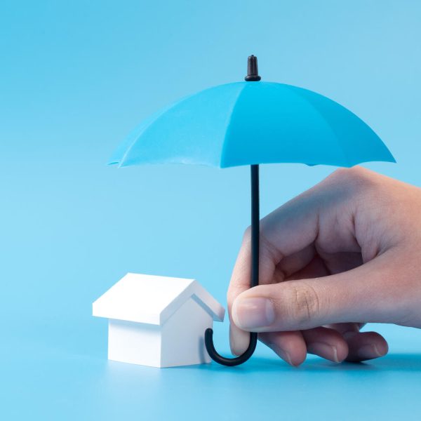 Home insurance or mortgage protection concept with a 3D house model under a blue umbrella