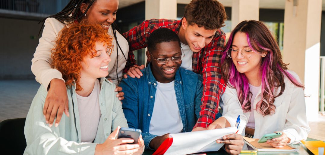 A diverse group of focused students actively collaborating on an exciting academic project with documents and devices, showcasing teamwork and engagement in a learning environment.
