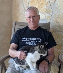 Ron Cody sitting in a chair with a cat in his lap. Ron is wearing a shirt that says "using Statistics to prove a point is just MEAN."